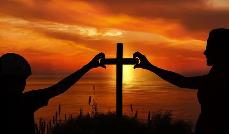 2 Menschen stehen links und rechts vor einem Christus-Kreuz vor einem Sonnenuntergang und formen mit ihren Händen je ein halbes Herz